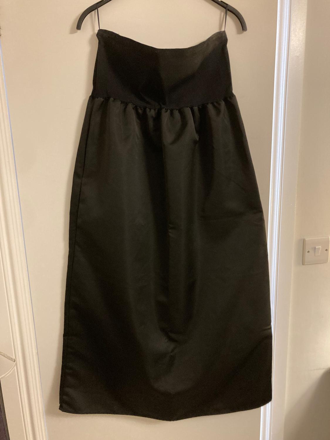 Strapless black dress hanging on a hanger over a white door. Smooth fabric and elegant drape.