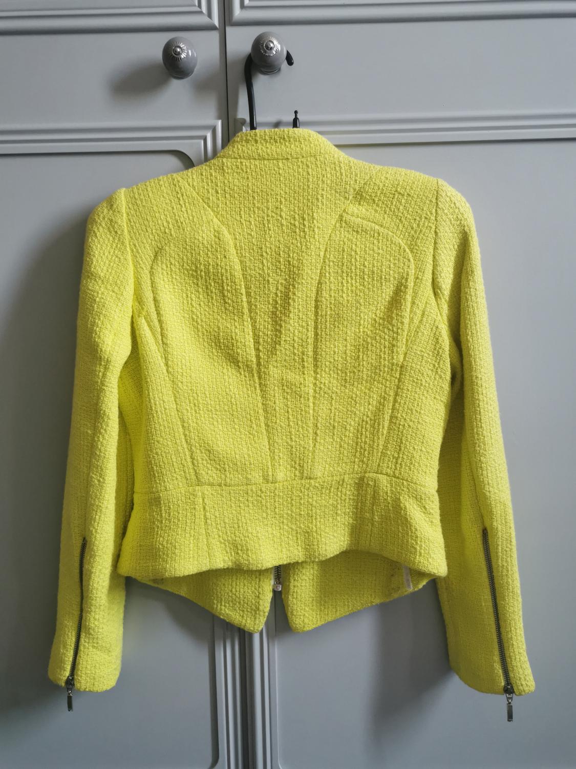 Rear view of a textured yellow jacket with zips on the sleeves.