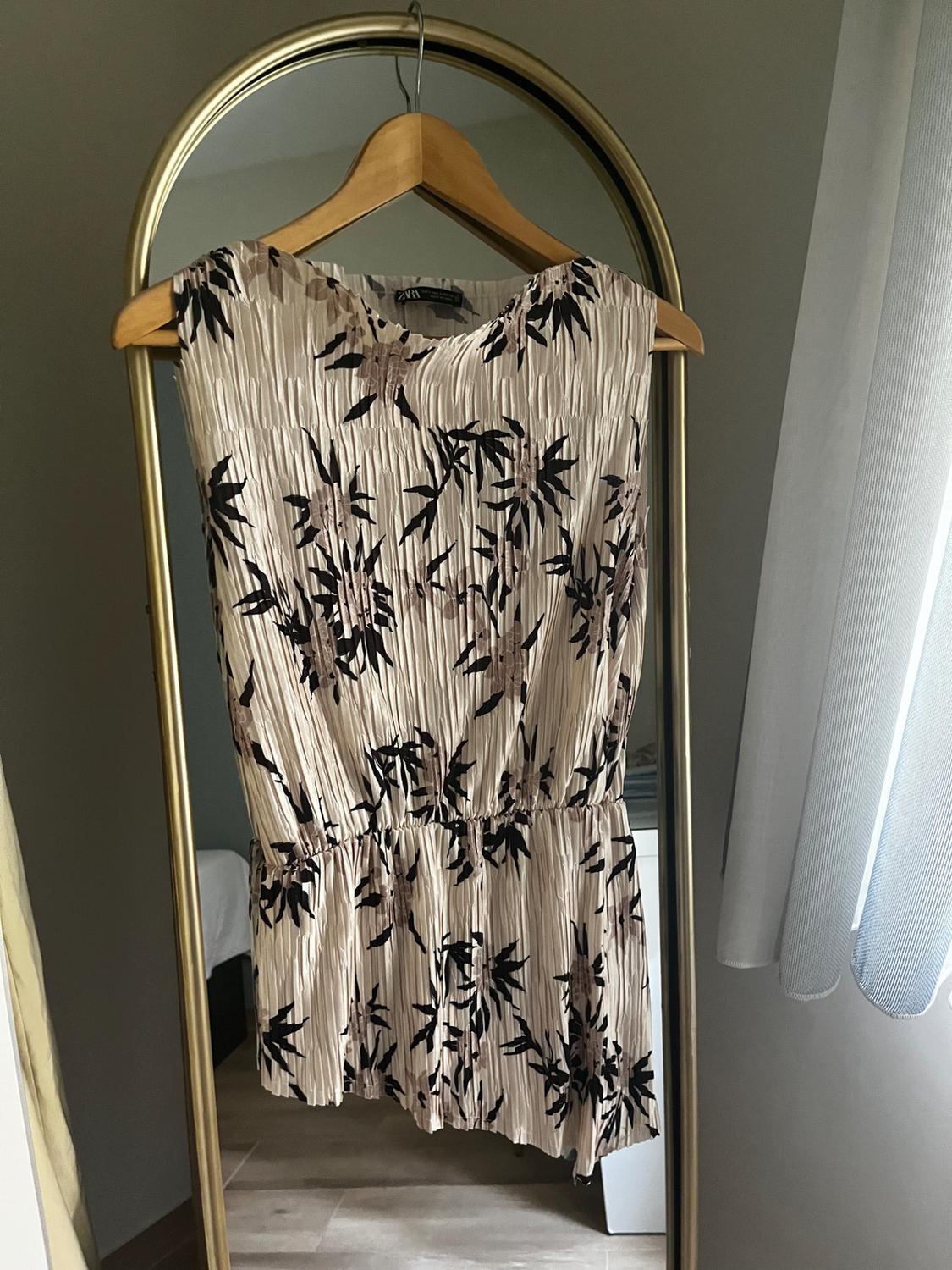 Pleated dress with black and beige floral print hanging on a gold-framed cheval mirror in a well-lit room.