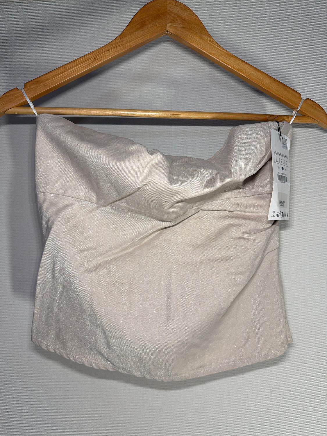 Shiny beige top hanging on a wooden hanger, with a visible tag on the right. Light gray background.