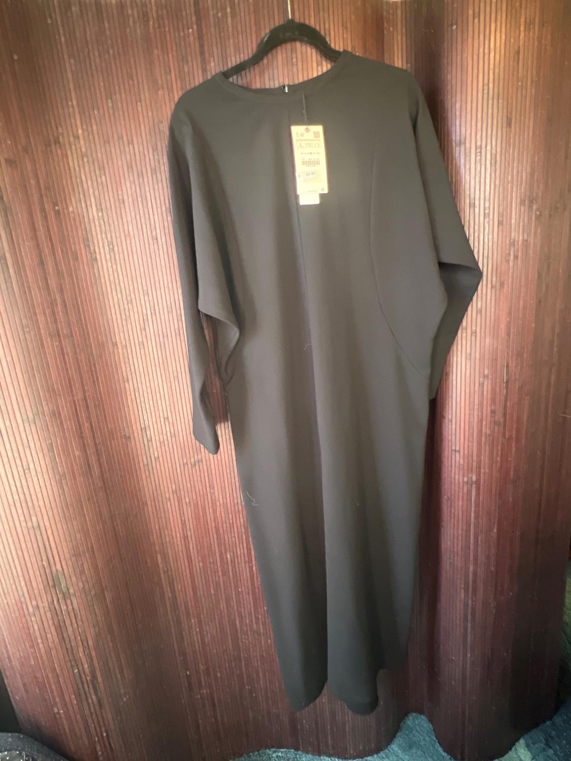 Long black dress hanging on a hanger in front of a wooden background. Visible tag at the top of the dress.
