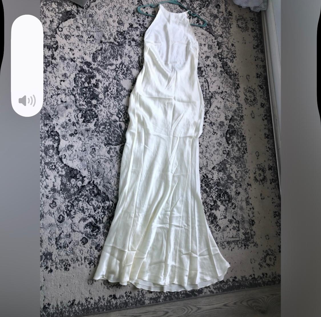 White sleeveless maxi dress on a rug with an abstract design in gray and black tones.