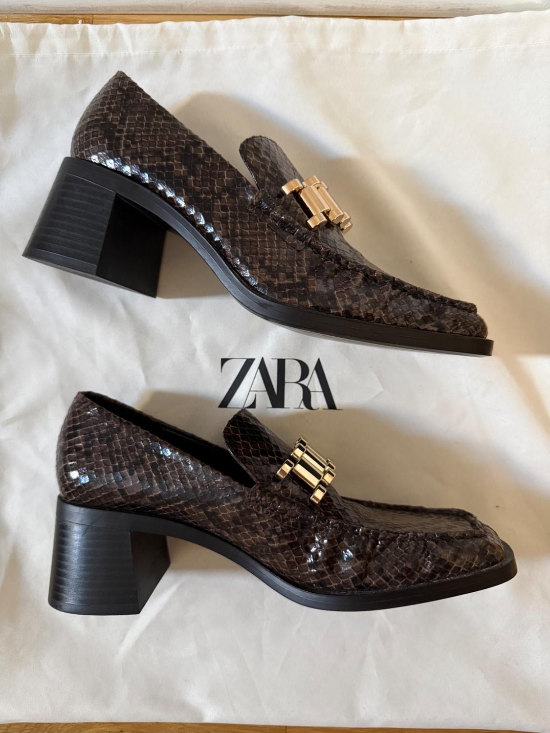 Brown block-heeled loafers with a snakeskin effect and gold metallic detail, resting on a white bag with the text ZARA.