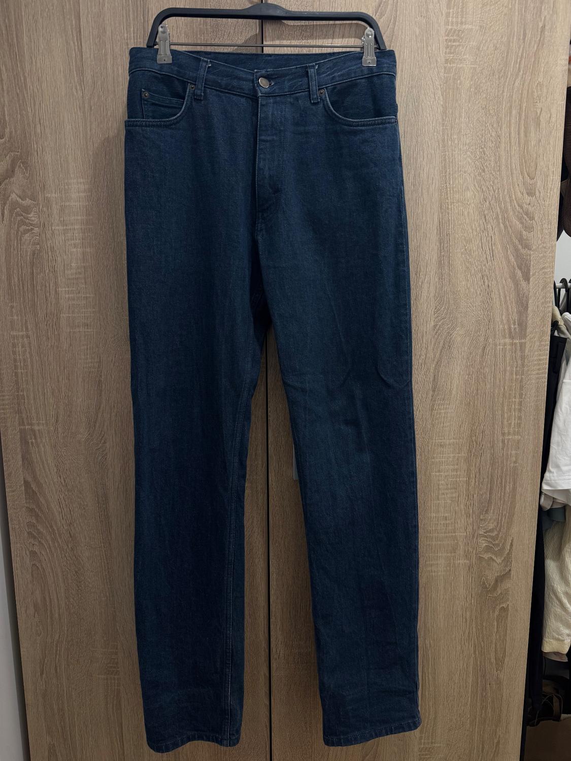 Dark blue jeans hanging on a hanger in front of a light wooden door.