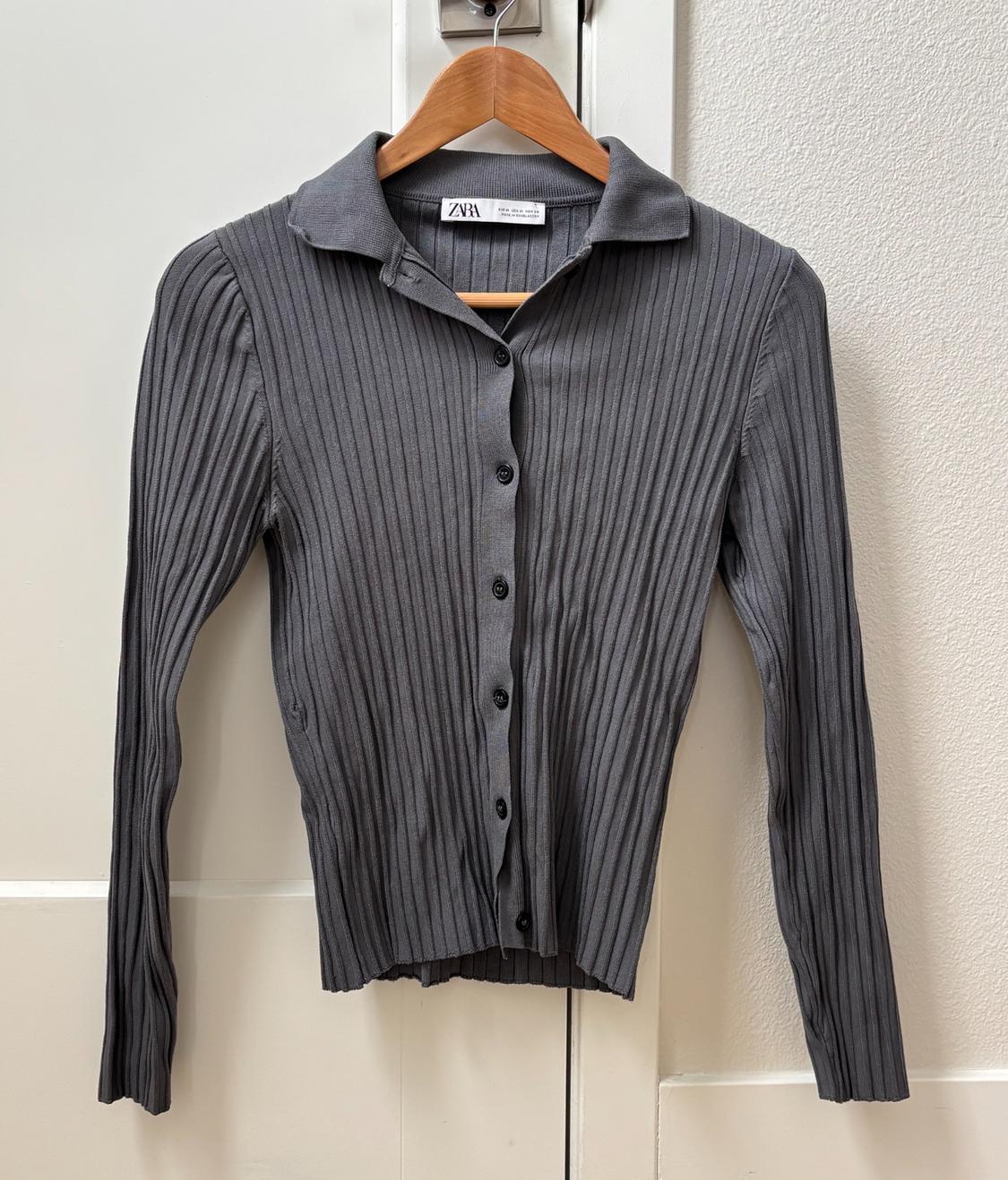Gray ribbed-knit cardigan with a collar and front buttons, Zara label, hanging on a wooden hanger over a white door.