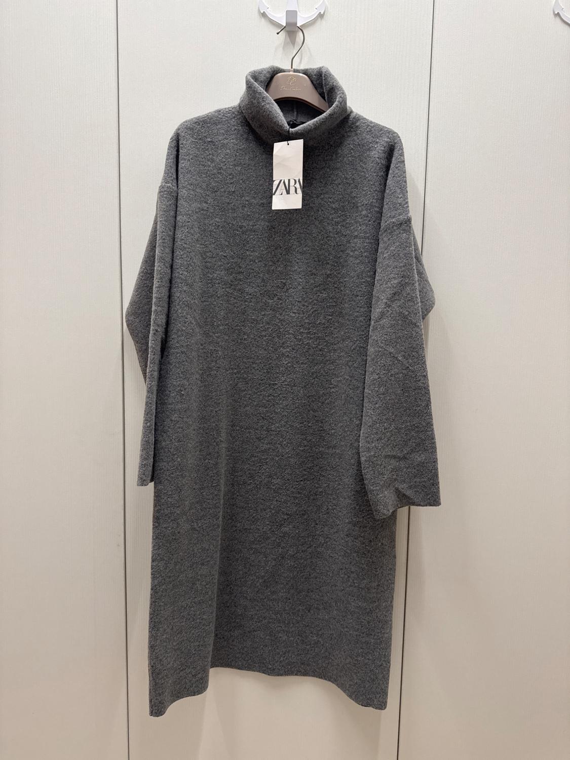 Grey knitted high-neck dress hanging on a hanger. Visible label with the text "ZARA". Light wall background.