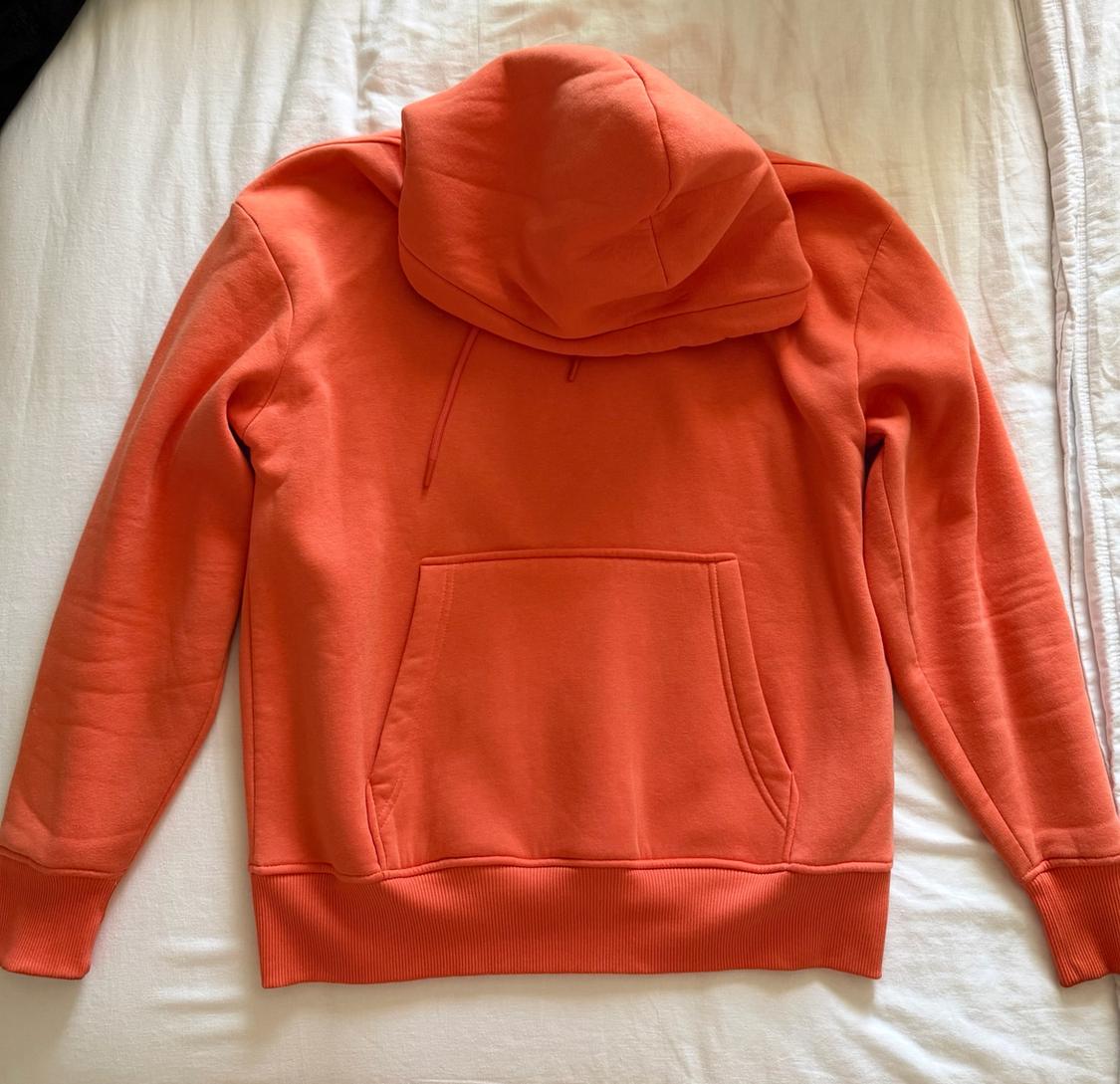 Orange hoodie with a kangaroo pocket, resting on a rumpled white sheet that gives it a casual and relaxed feel.