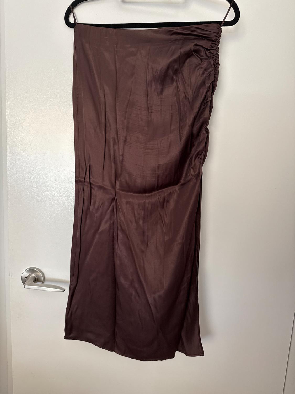 Brown satin skirt with side ruching, hanging on a black hanger over a white door with a silver door handle. Casual style.