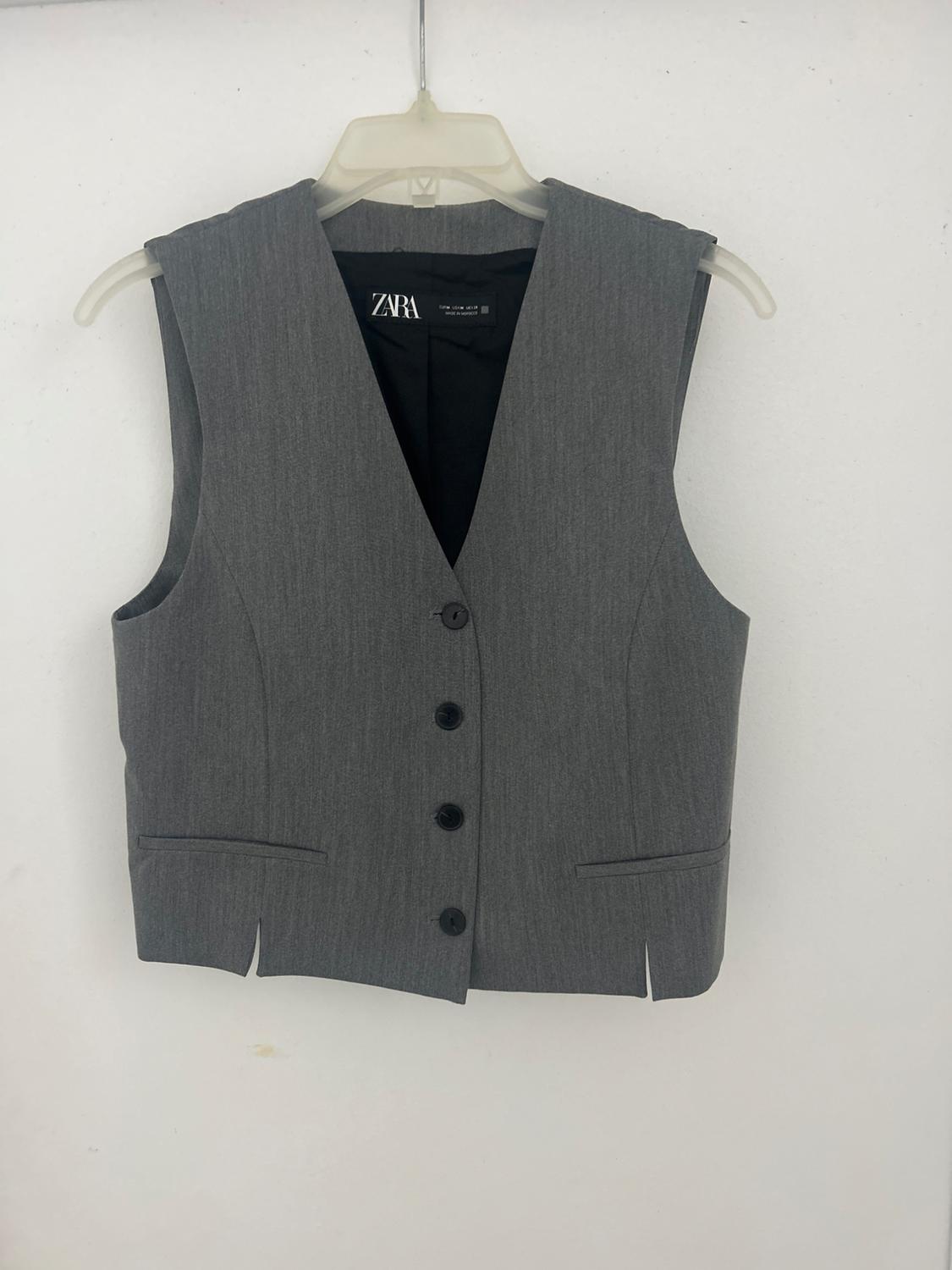 Gray sleeveless vest with three black buttons, hanging on a white hanger. Visible tag: "ZARA". White background.