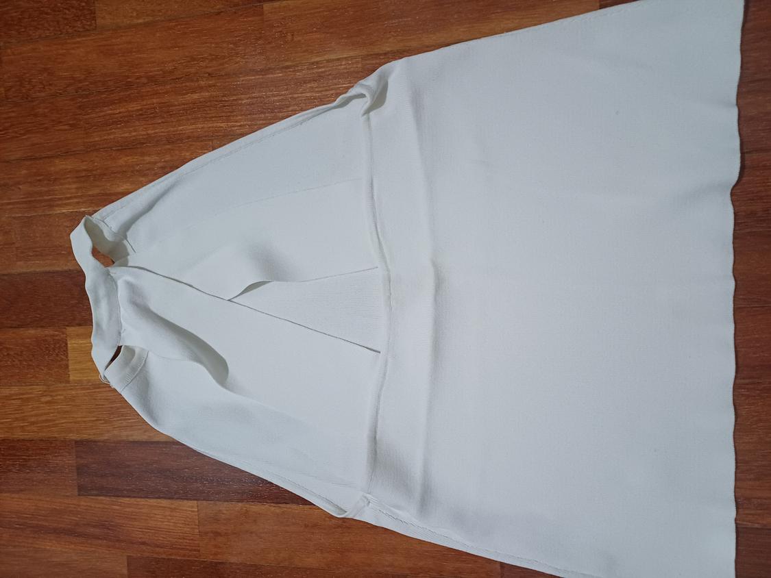 Detail of a white blouse with a round neck and no sleeves.