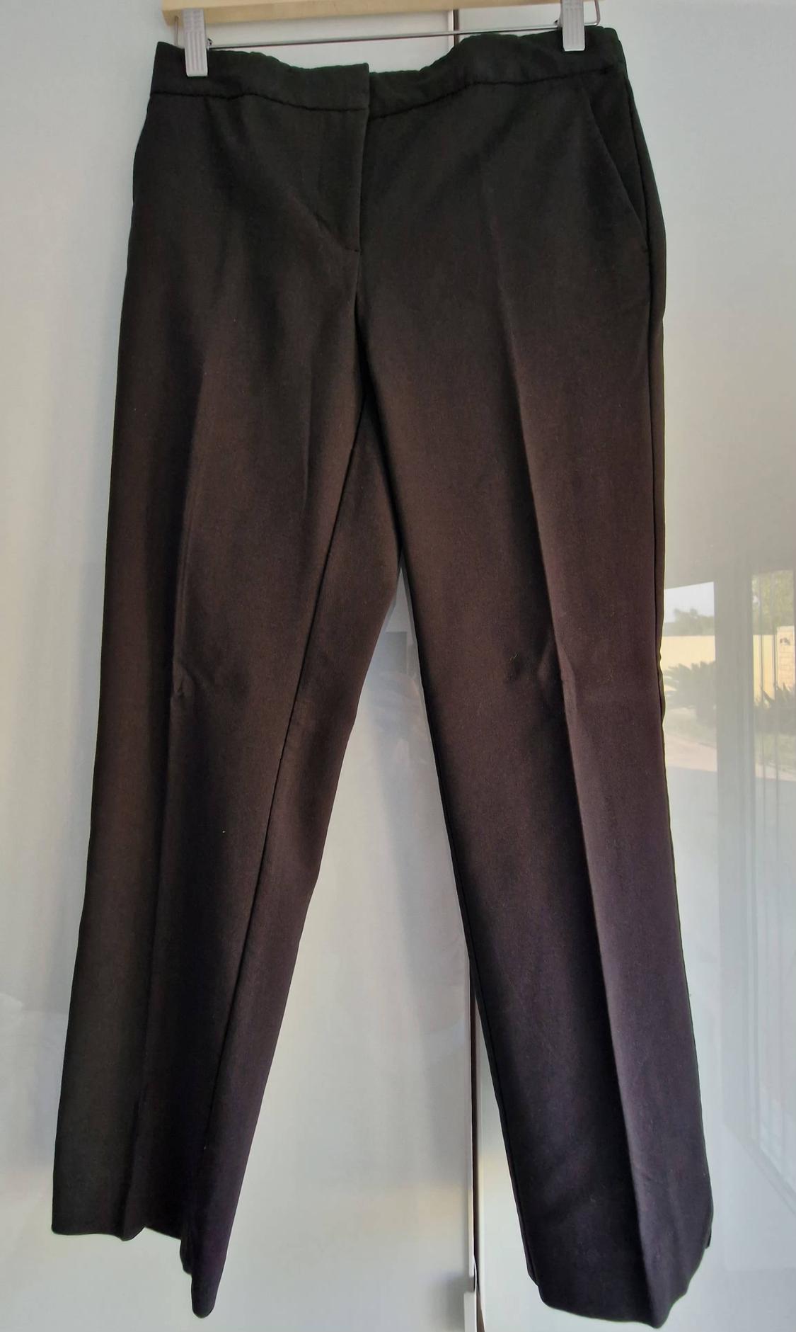 Dark trousers hanging on a hanger against a bright white background with the reflection of a window.