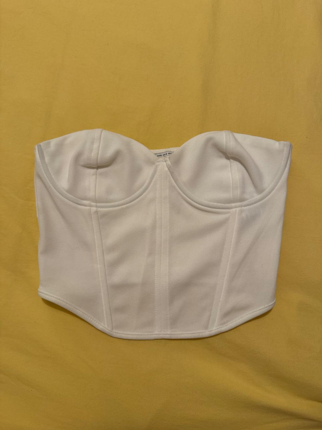 White corset on a yellow background, with structured cups and visible seams.