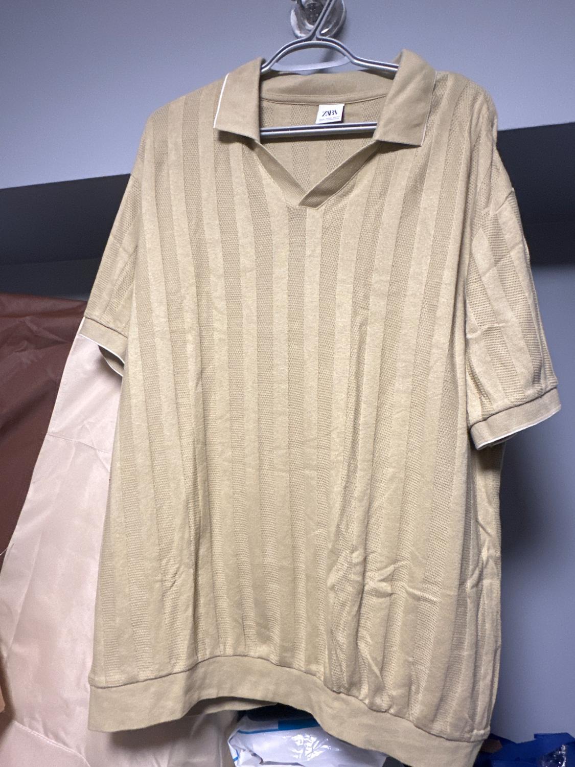 Front view of a beige polo shirt with short sleeves, featuring raised vertical stripes.