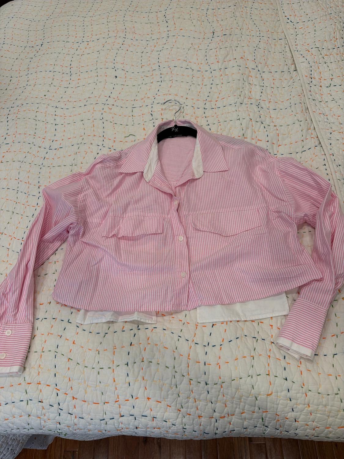Short-sleeved pink and white striped shirt with pockets and a white hem, on a hanger resting on a quilt with colorful stitching.