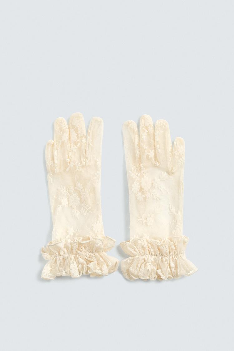 Frontalt bilde av råhvite, halvtransparente hansker med blomsterjacquard og volanger på håndleddene.