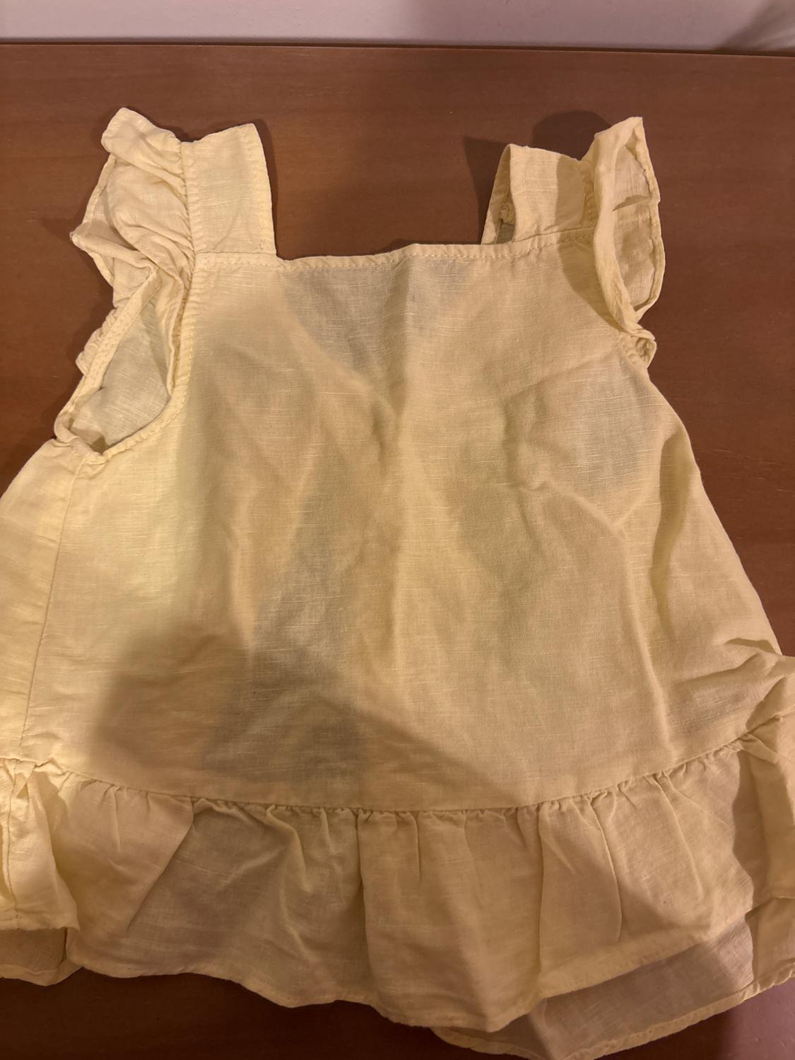 Yellow camisole with ruffles on the shoulders and hem, on a wooden surface.
