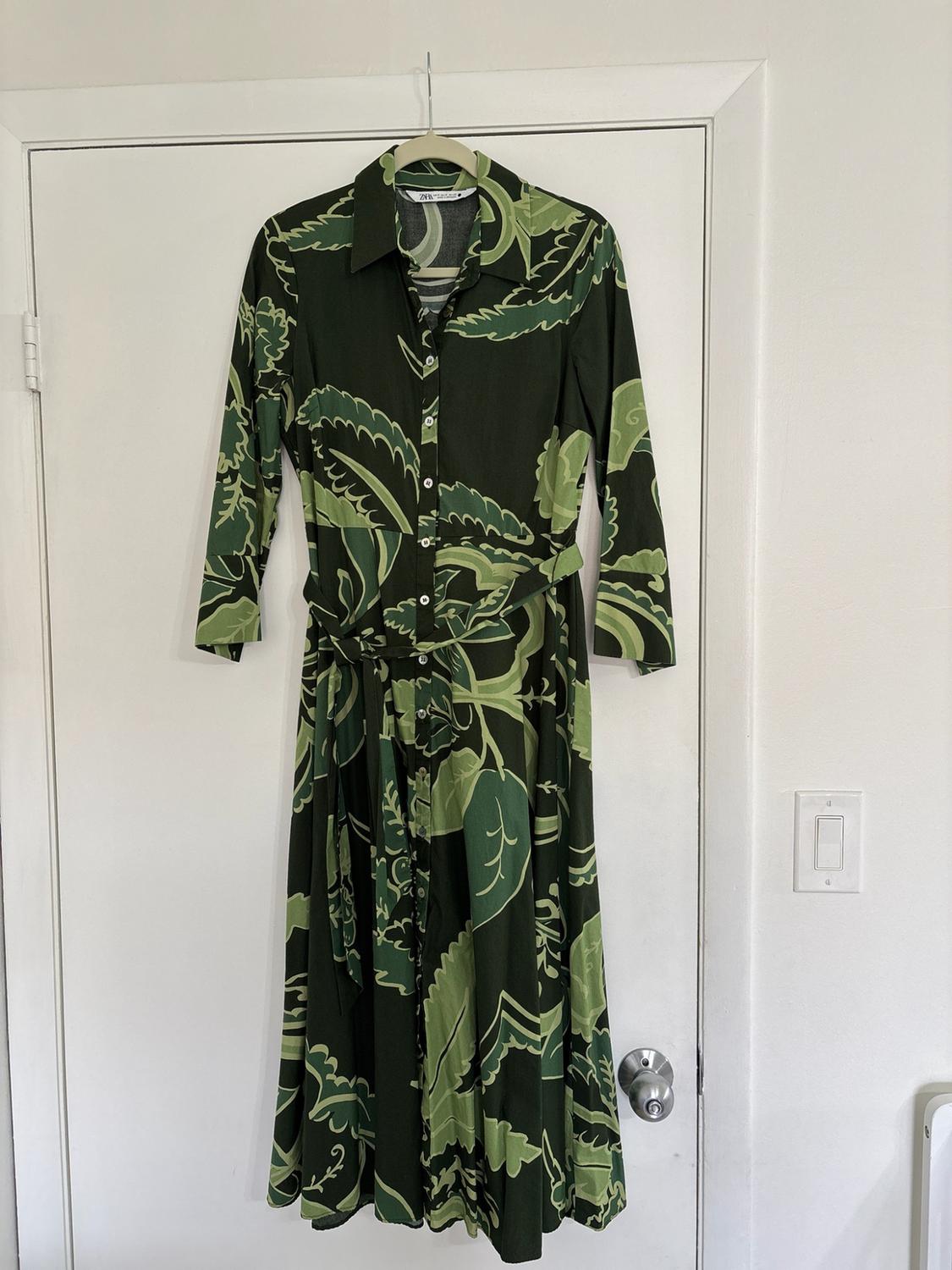 Dark green long shirt dress with a leaf print and belt, hanging on a white door in a relaxed, homely setting.