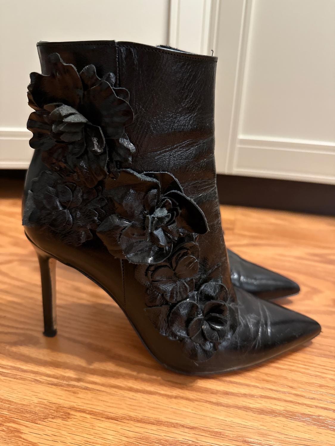 Black high-heeled ankle boots with embossed floral details, on a light wooden floor.