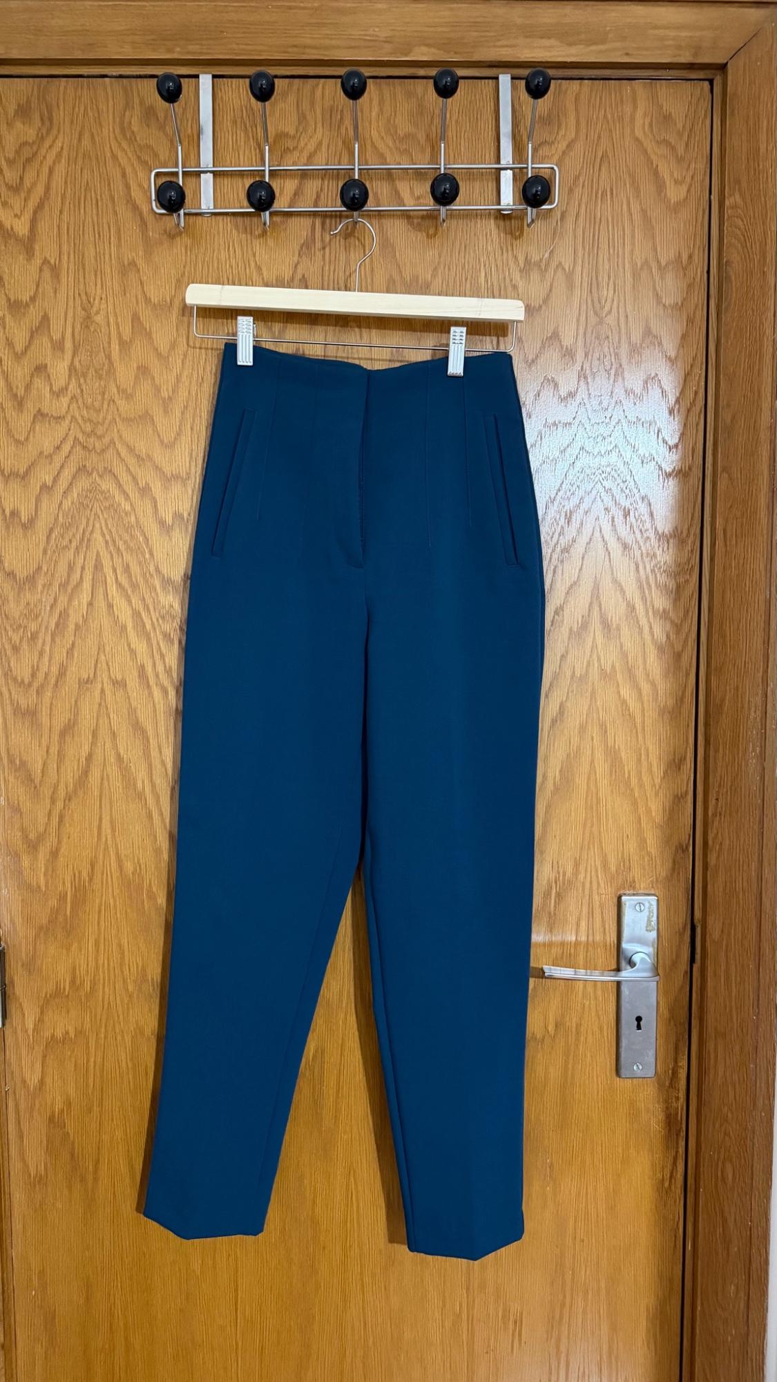Dark blue trousers hanging from a hanger on a metal clothes rack above a wooden door.