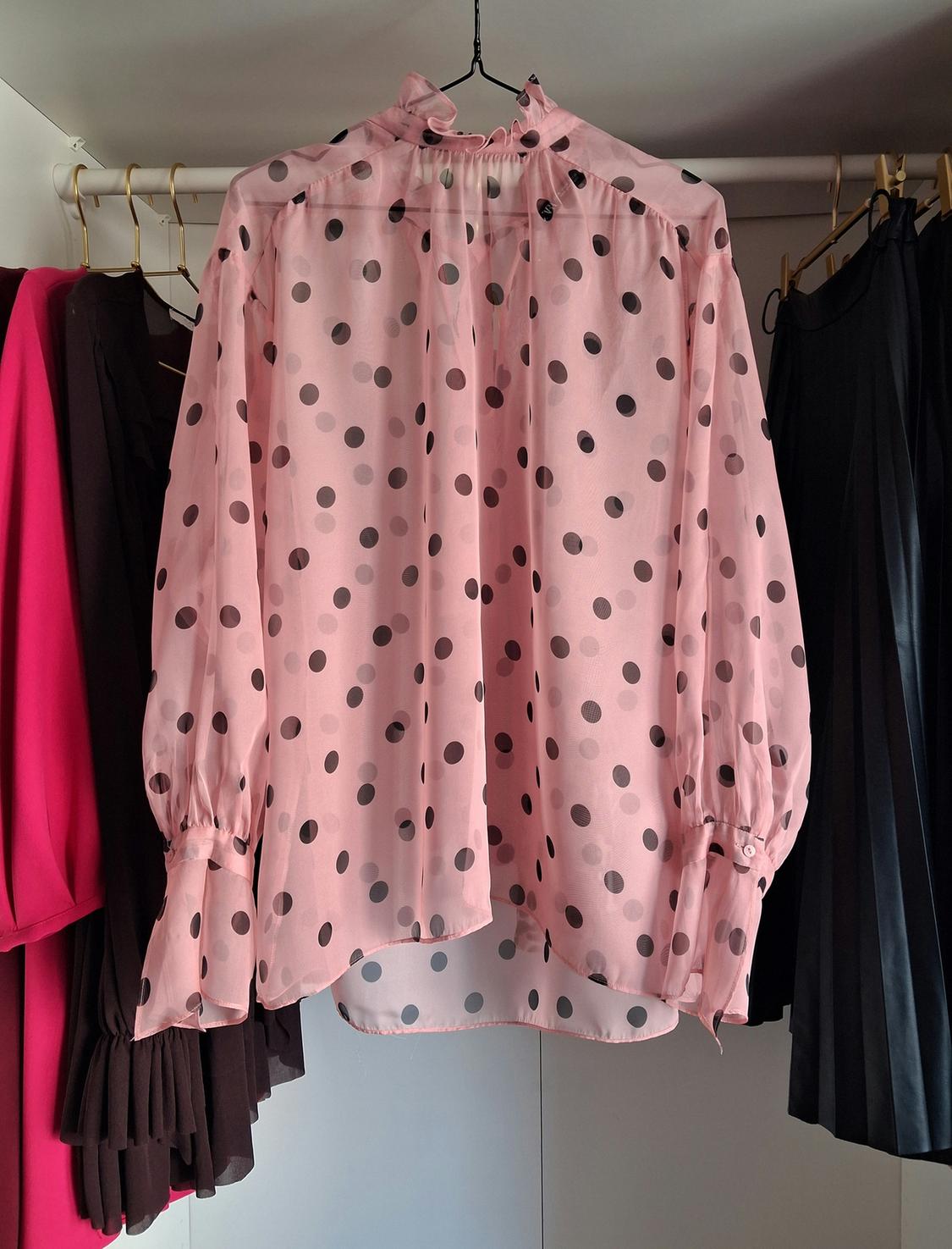 Pink blouse with black polka dots hanging in a wardrobe, surrounded by other dark-coloured and fuchsia garments.