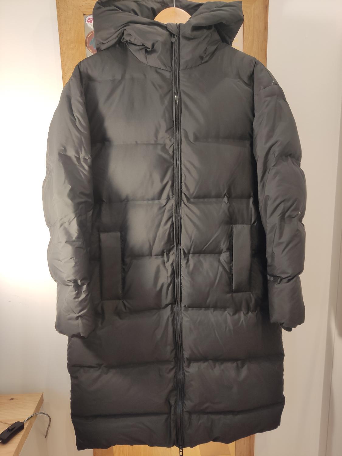 Front view of a black padded hooded coat with side pockets.