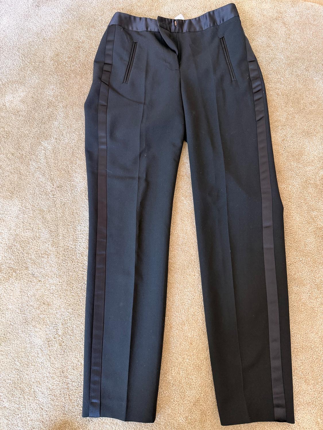 Black trousers with satin side stripes, front pockets, and button fastening, on a beige rug.