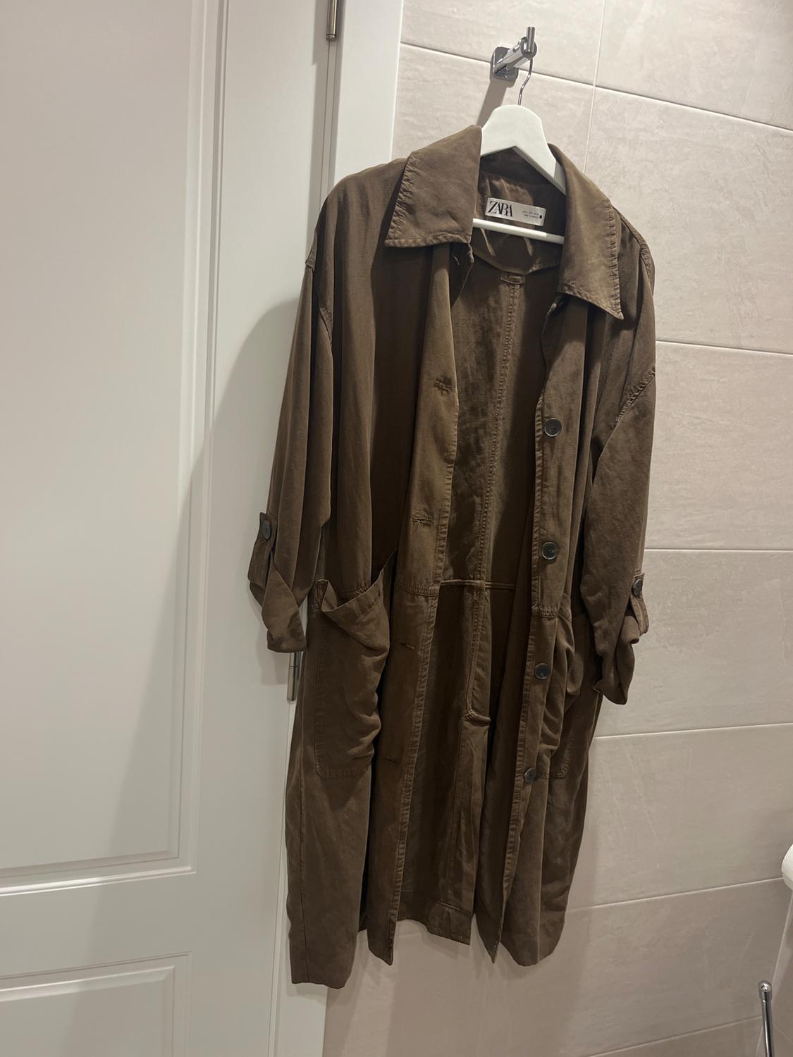 Brown coat hanging on a white hanger over a white door. Visible label with the text "ZARA". Light tiled background.