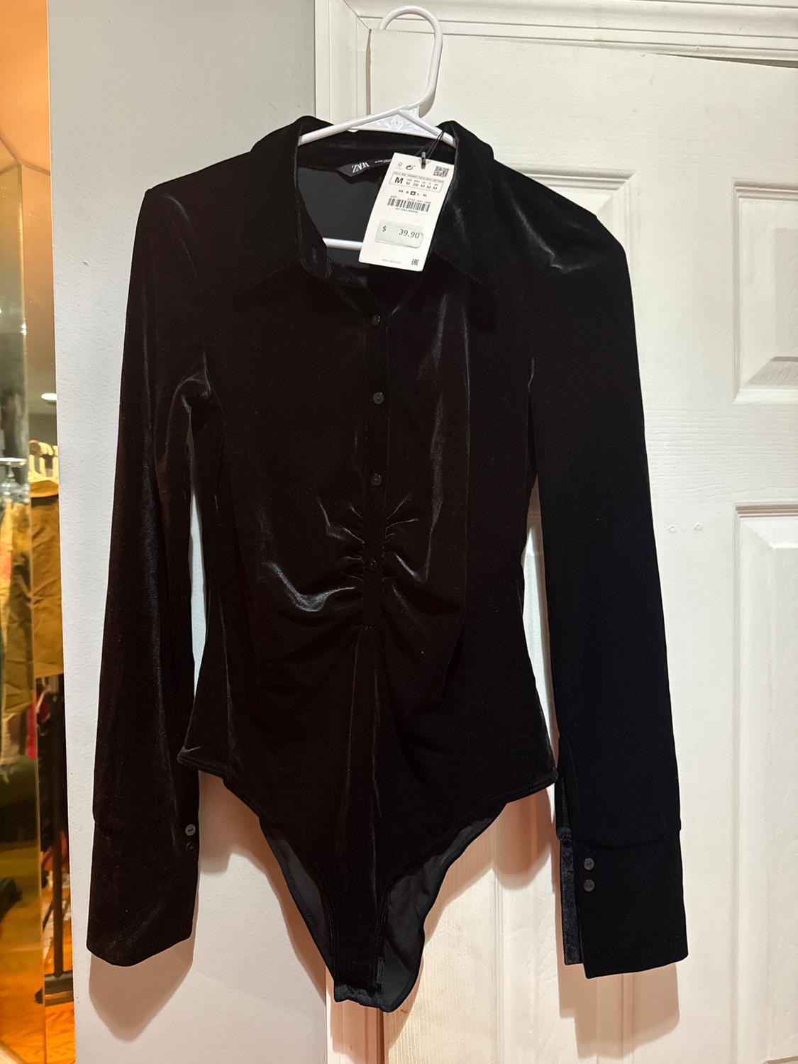 Black velvet bodysuit with long sleeves and buttons, hanging on a white hanger. Visible tag with price of $39.90.