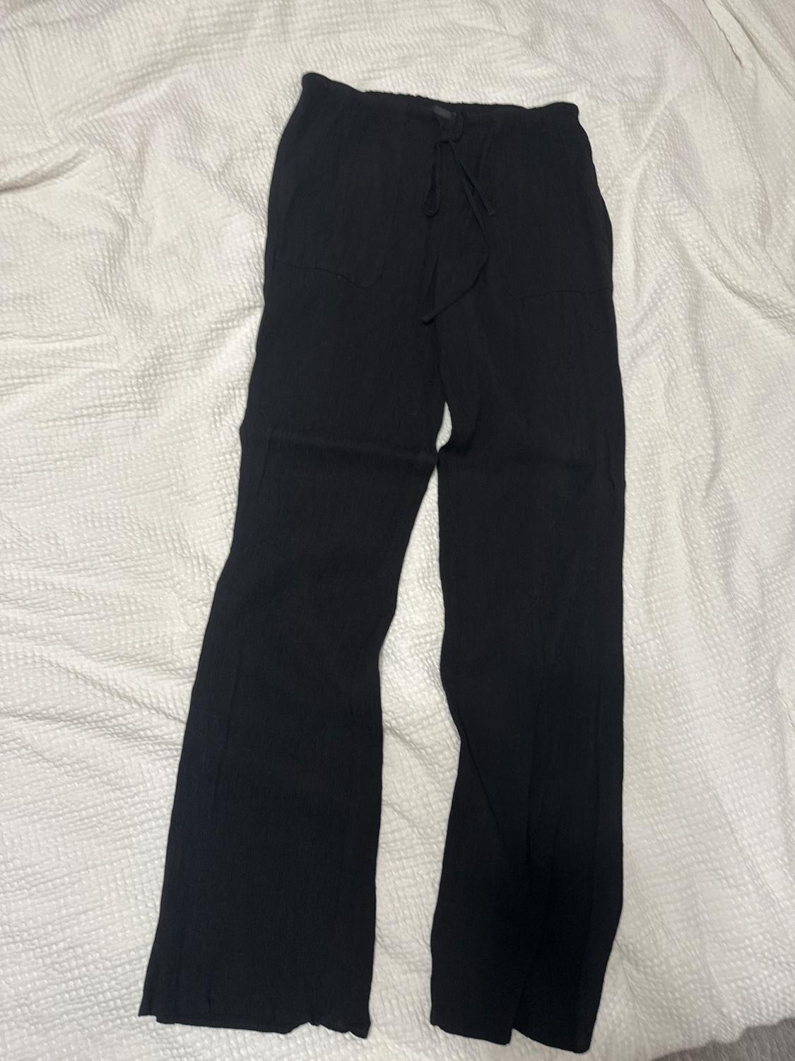 Front view of black trousers with front pockets and a drawstring waist.