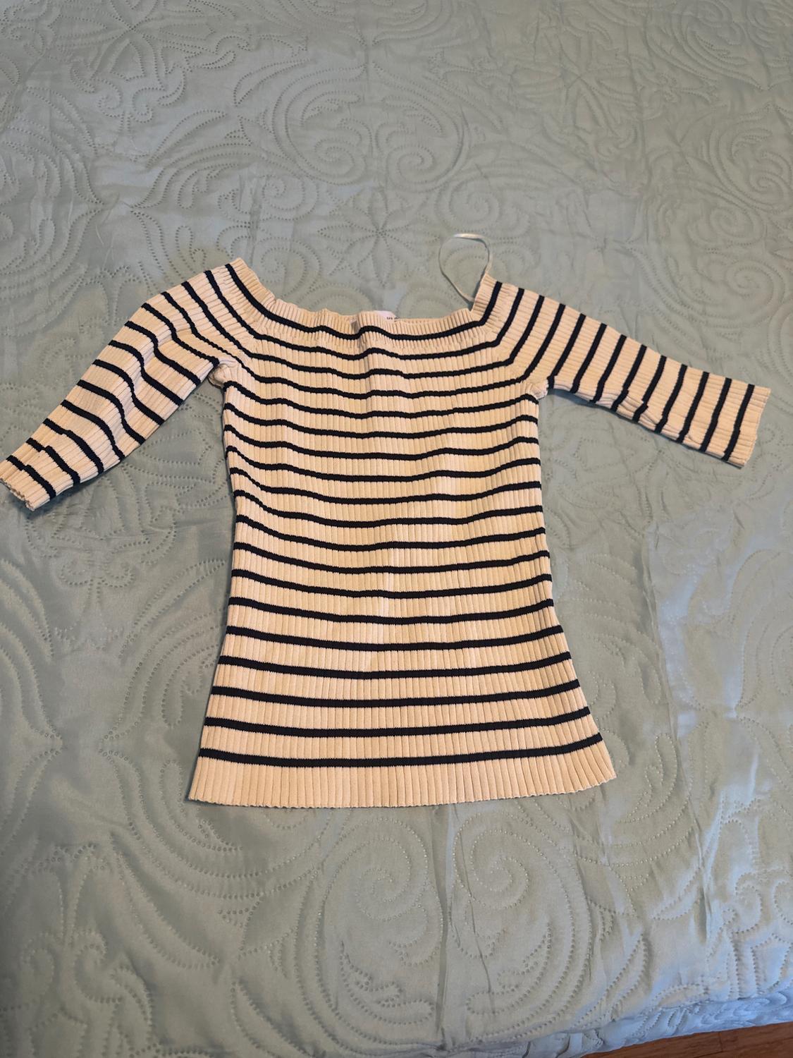 Black and white horizontal striped ribbed knit top with a boat neckline and three-quarter sleeves, laid on a textured light blue bedspread.