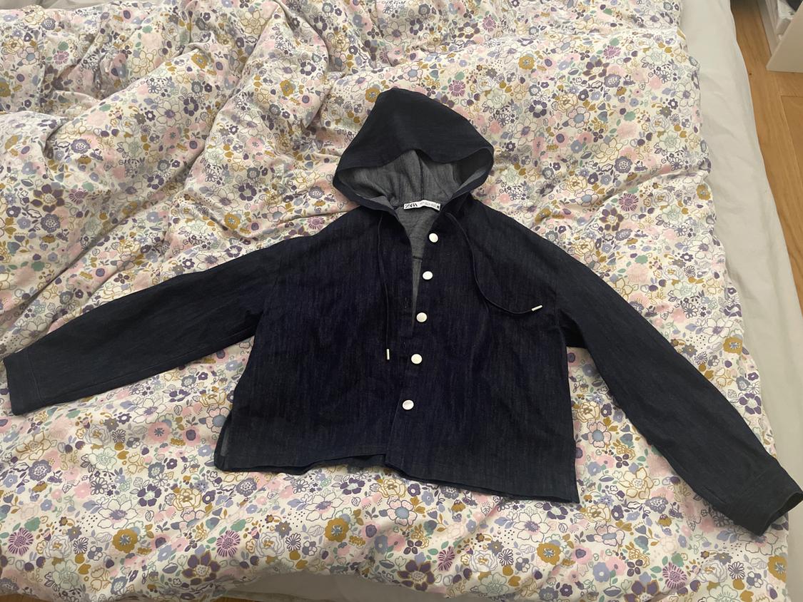 Black hooded jacket with white buttons on a bed with a pastel-coloured floral bedspread.