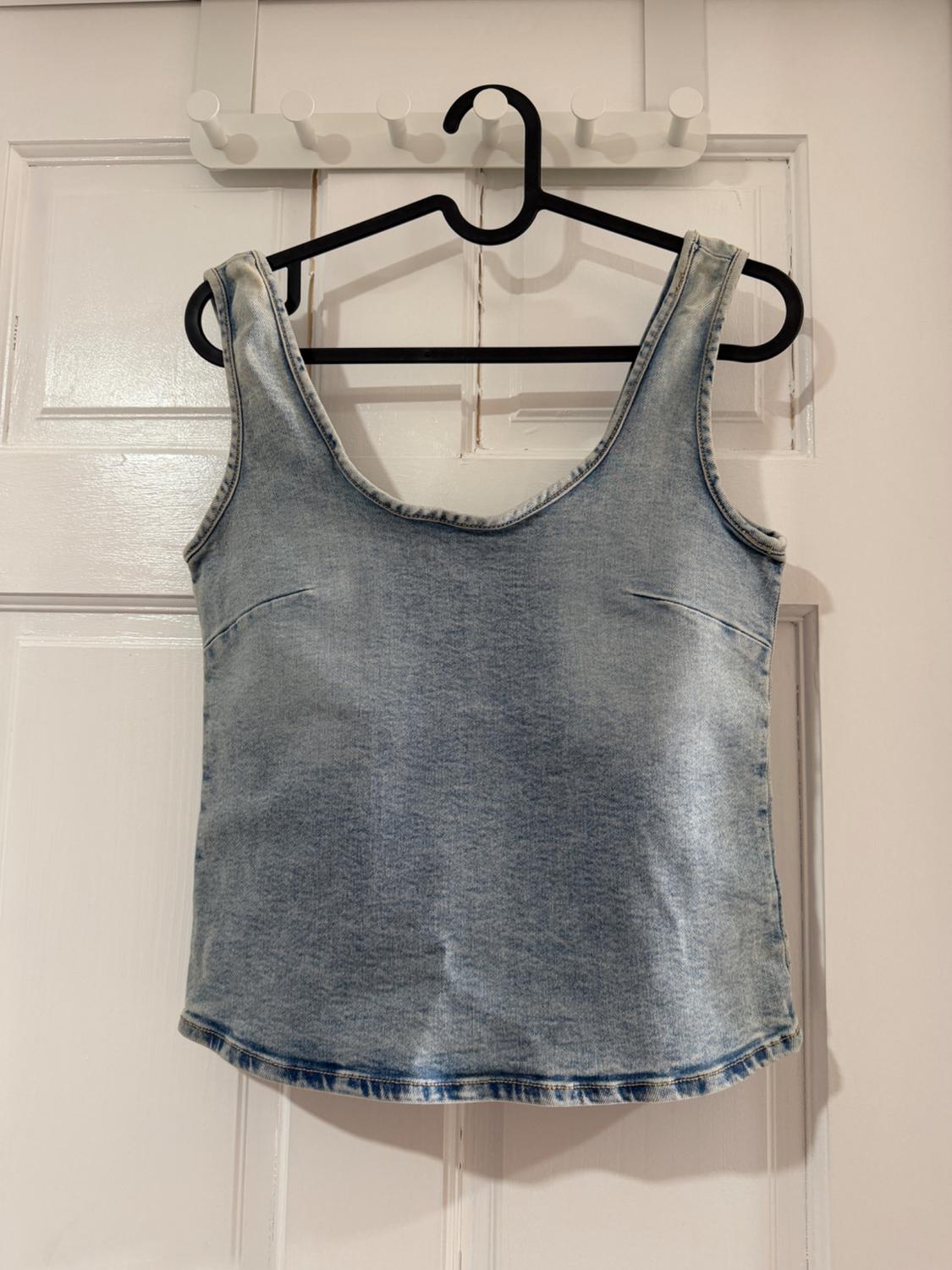 Light blue denim top hanging on a black hanger over a white door.