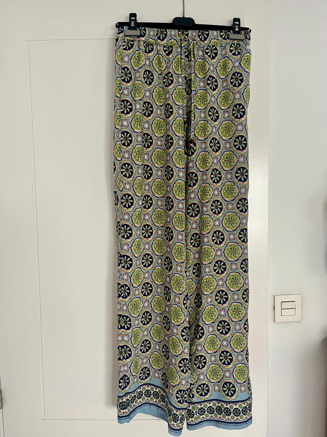 Trousers hanging with geometric print in shades of green, blue and white, on a white background.