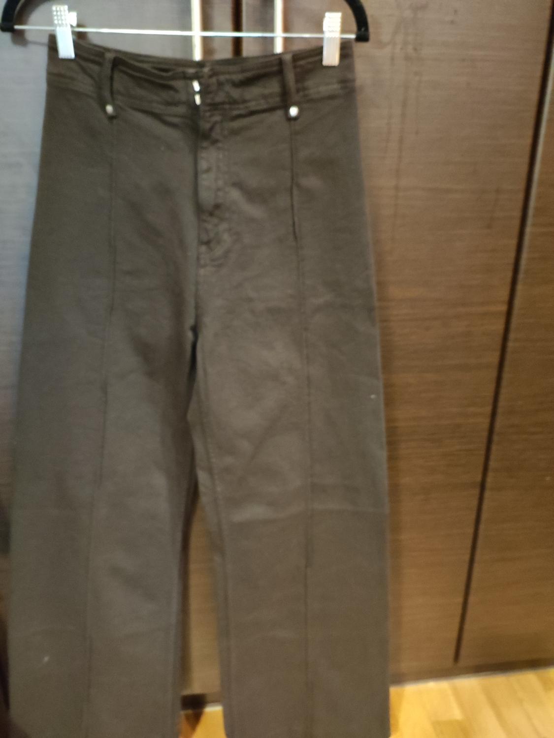 Dark trousers hanging on a hanger against a wooden background. The image shows stitching and pocket details.