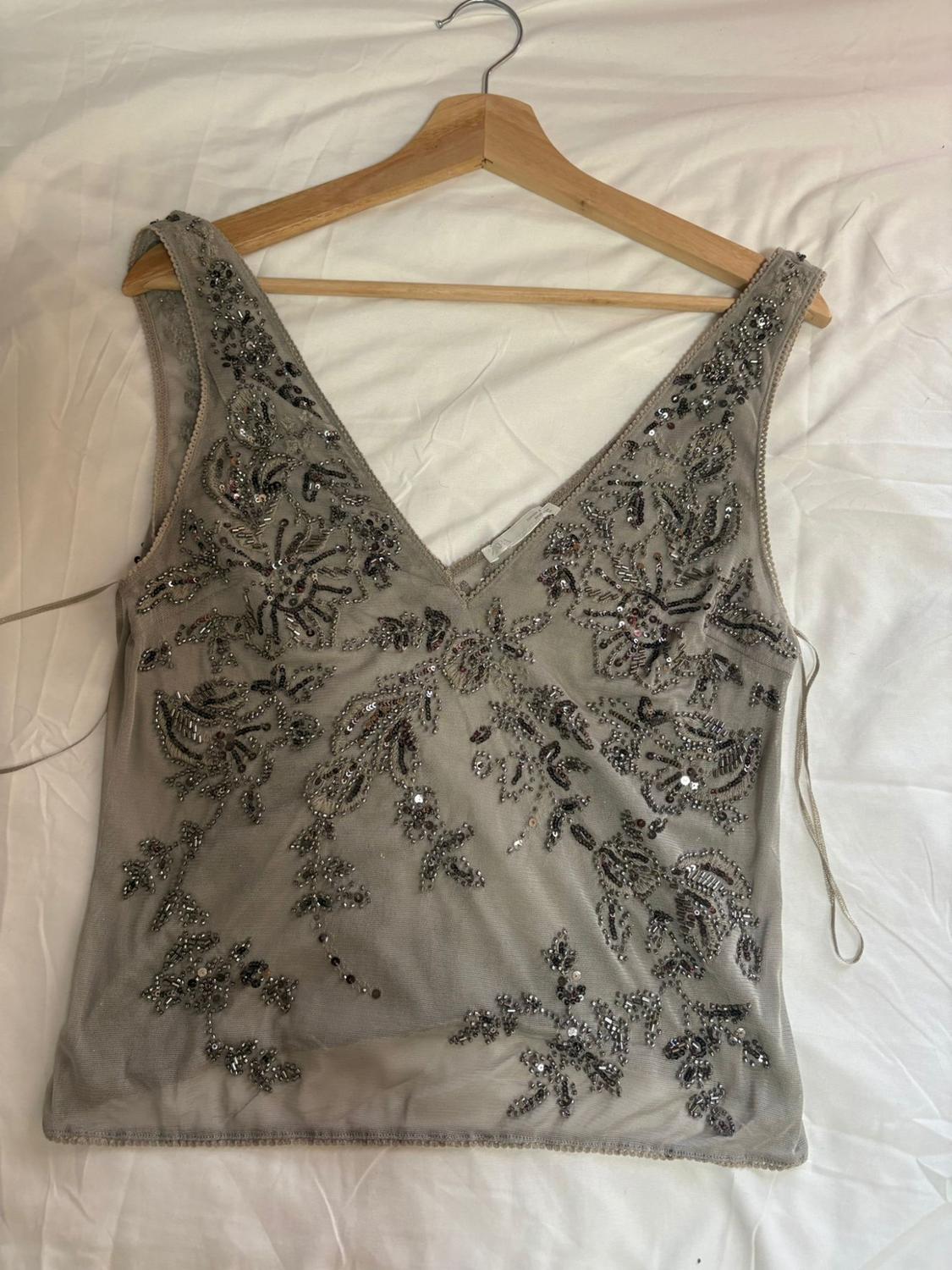 Semi-transparent grey top with a V-neck, sequins and floral beads, on a wooden hanger over a white sheet.