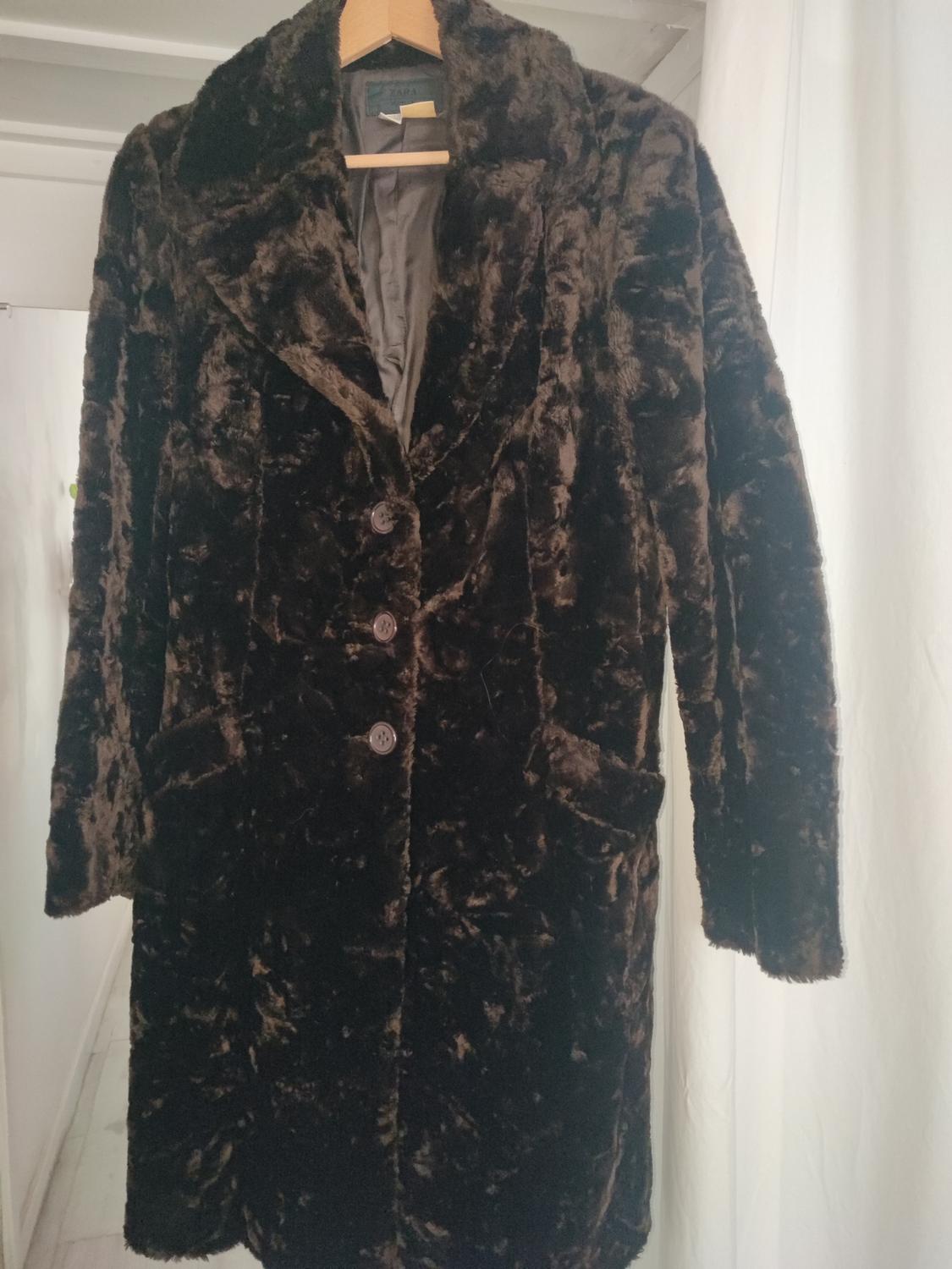 Dark brown faux fur coat hanging on a wooden hanger, with front buttons and side pockets.