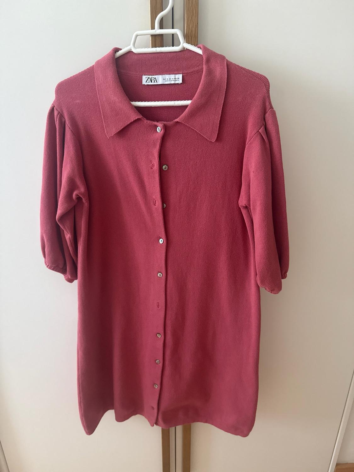 Pink knitted dress with a collar, front buttons and puff sleeves, hanging on a clothes hanger against a white background. Visible text: ZARA.