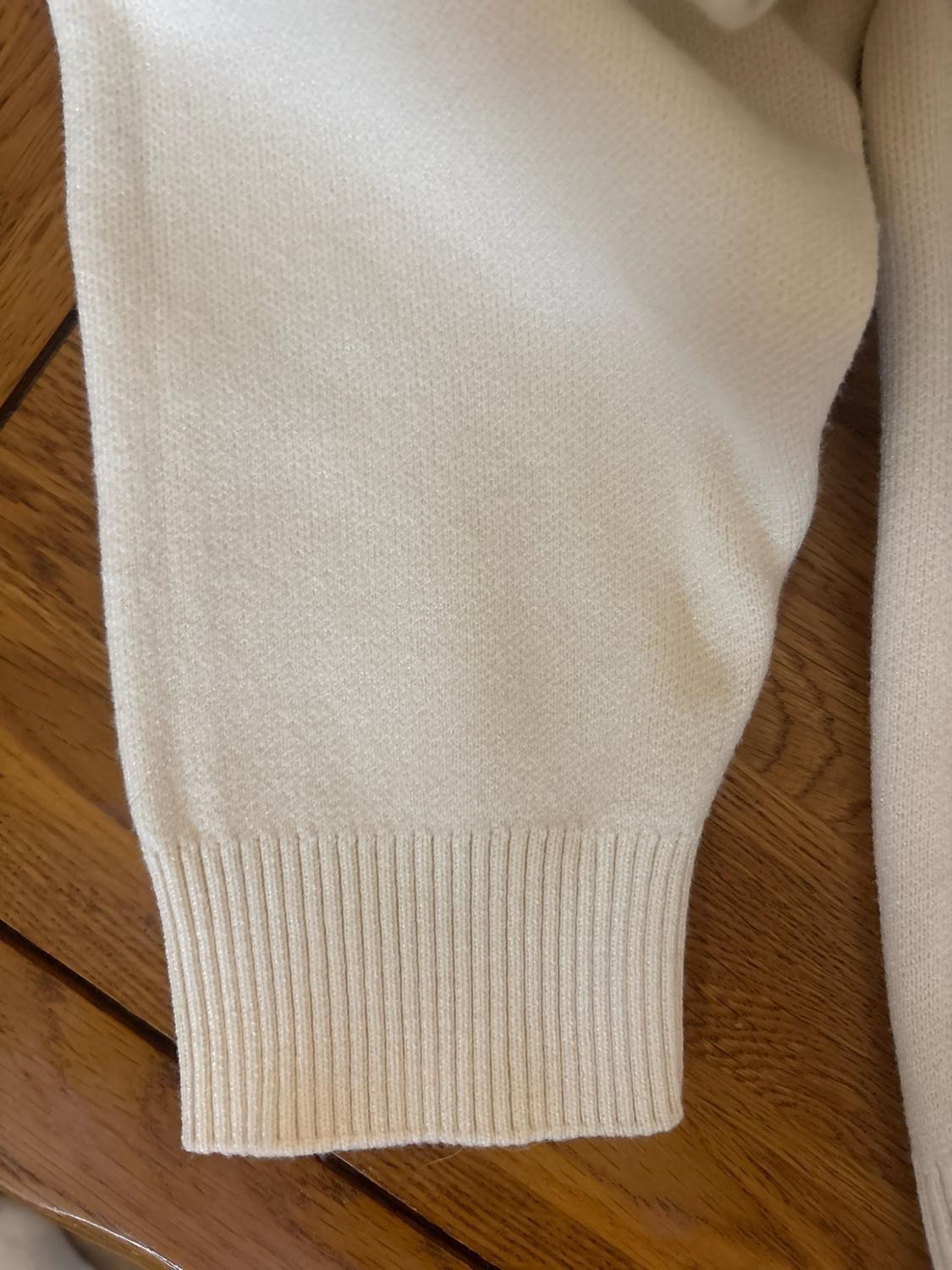 Close-up of the sleeve of a cream knitted jumper with a ribbed cuff on a wooden surface.