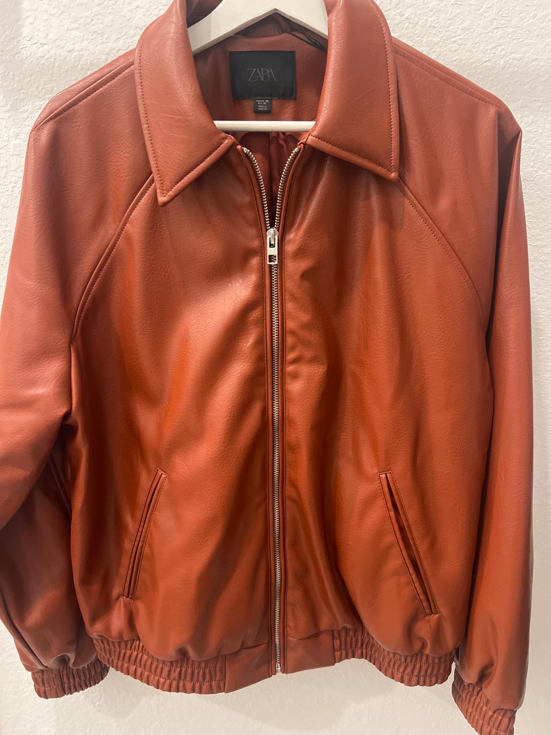 Brown jacket with zip and classic collar, hanging on a white hanger. Visible label with the ZARA brand.