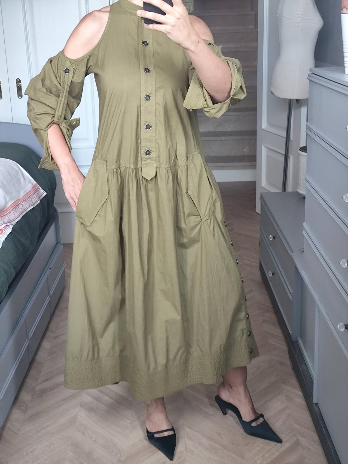 Woman taking a selfie in a room mirror, wearing an olive green off-the-shoulder midi dress and black shoes.