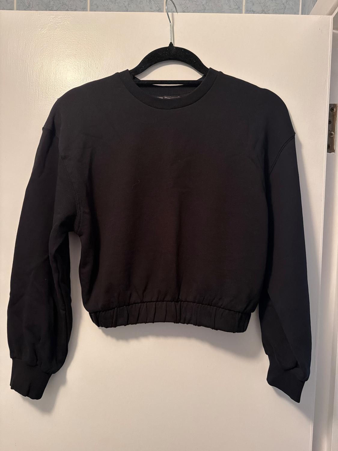 Black long-sleeved sweatshirt hanging on a black hanger over a white door.