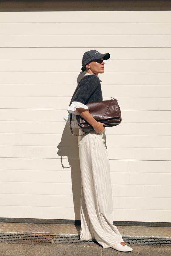 Souprava širokých bílých kalhot s proužky, bílé halenky s volánky a tmavě šedého svetru.