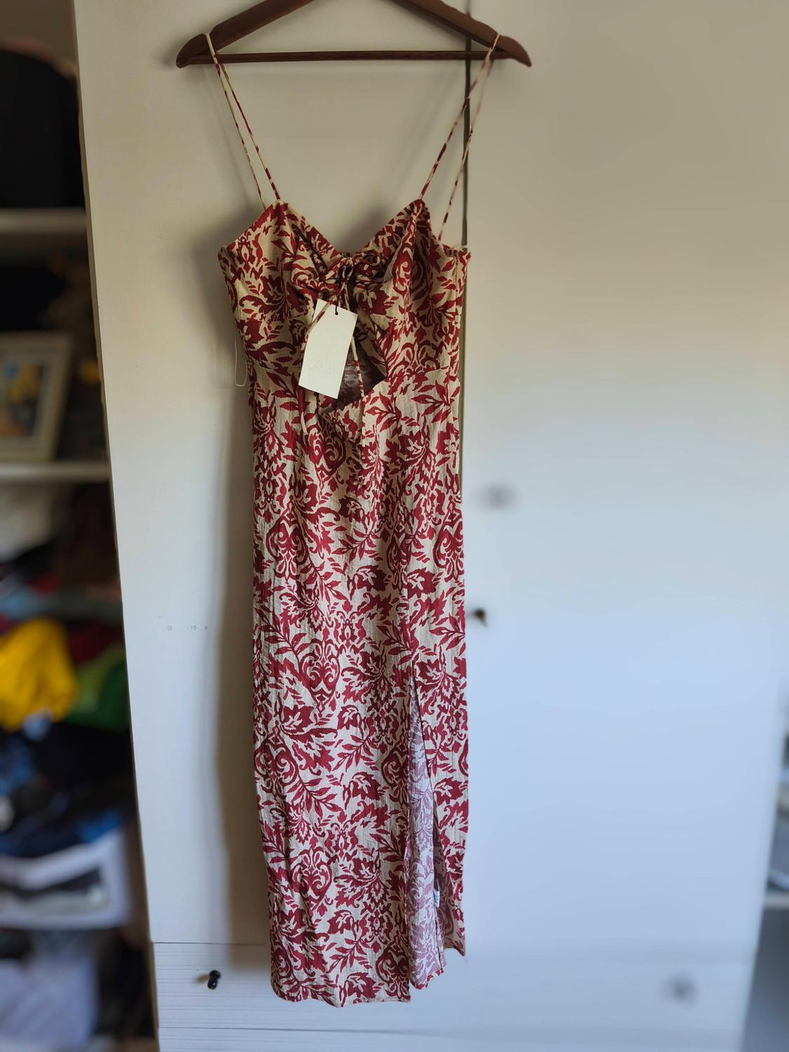 Long strappy dress with a red floral print on a cream background. It features a front slit and a leg slit, hanging in a white wardrobe.
