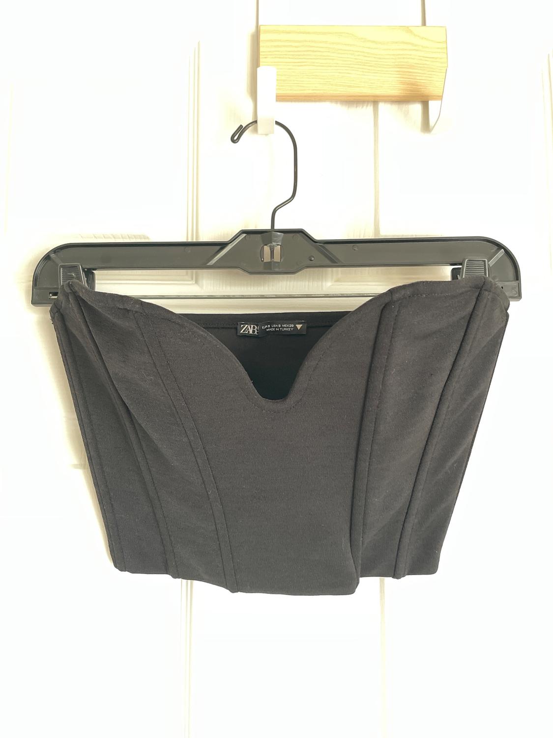 Black top hanging on a black hanger over a white door. Visible label with text: "Zara".
