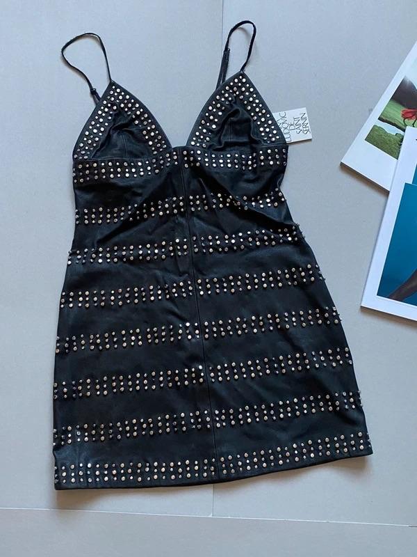 Black dress with thin straps and stud embellishments in horizontal rows. Grey background with partially visible magazines.