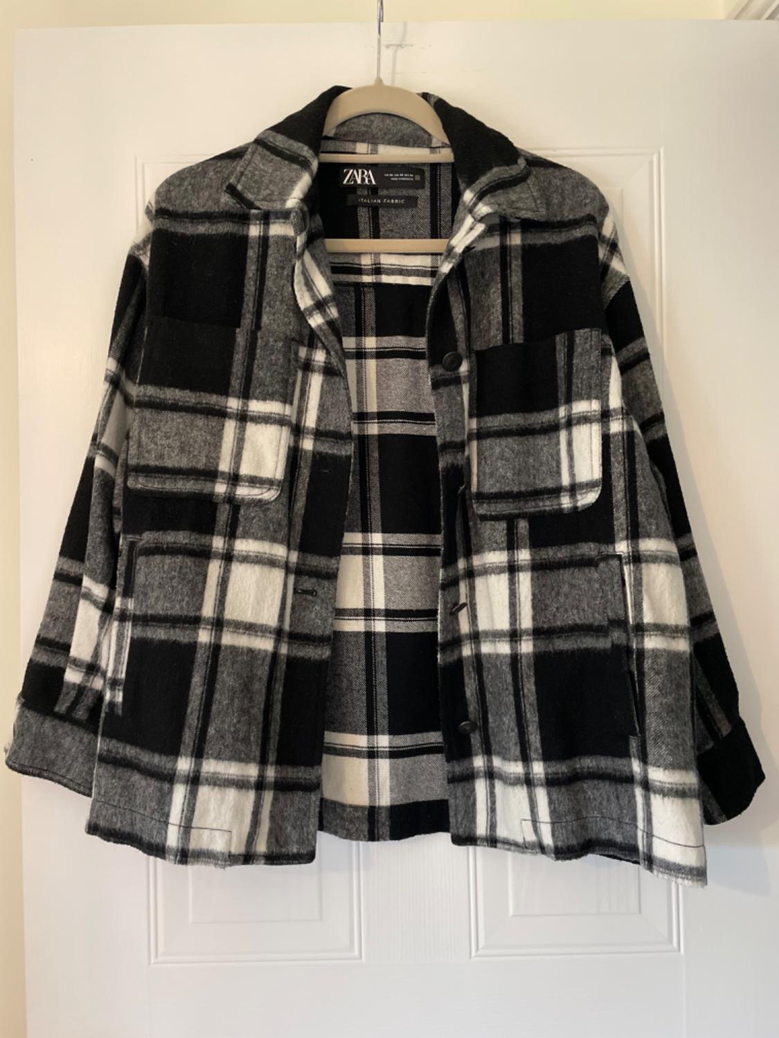 Front view of a black, white, and grey checked jacket with front pockets and buttons.