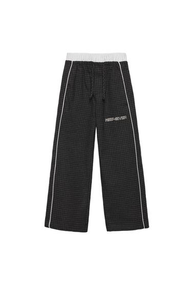 Μπροστινή όψη μαύρου παντελονιού με λευκή ελαστική μέση, κείμενο 'KEEP4EVER' και λευκές κάθετες γραμμές.
