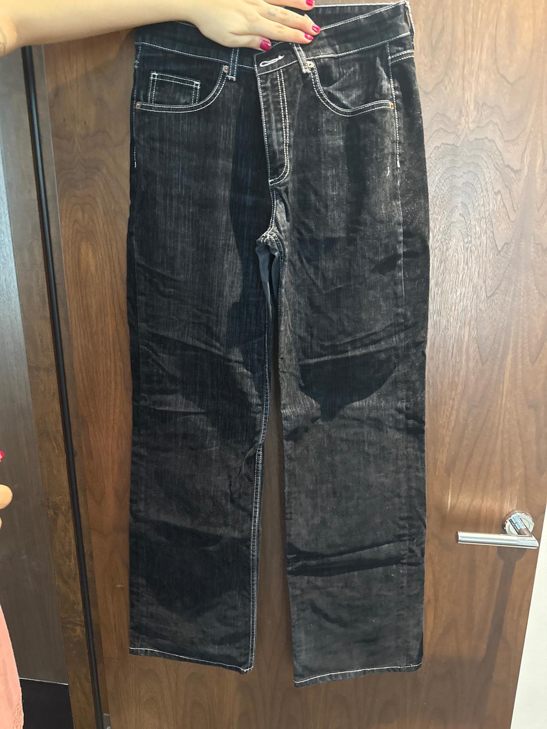Black jeans hanging from a wooden door, held by a hand with pink painted nails.
