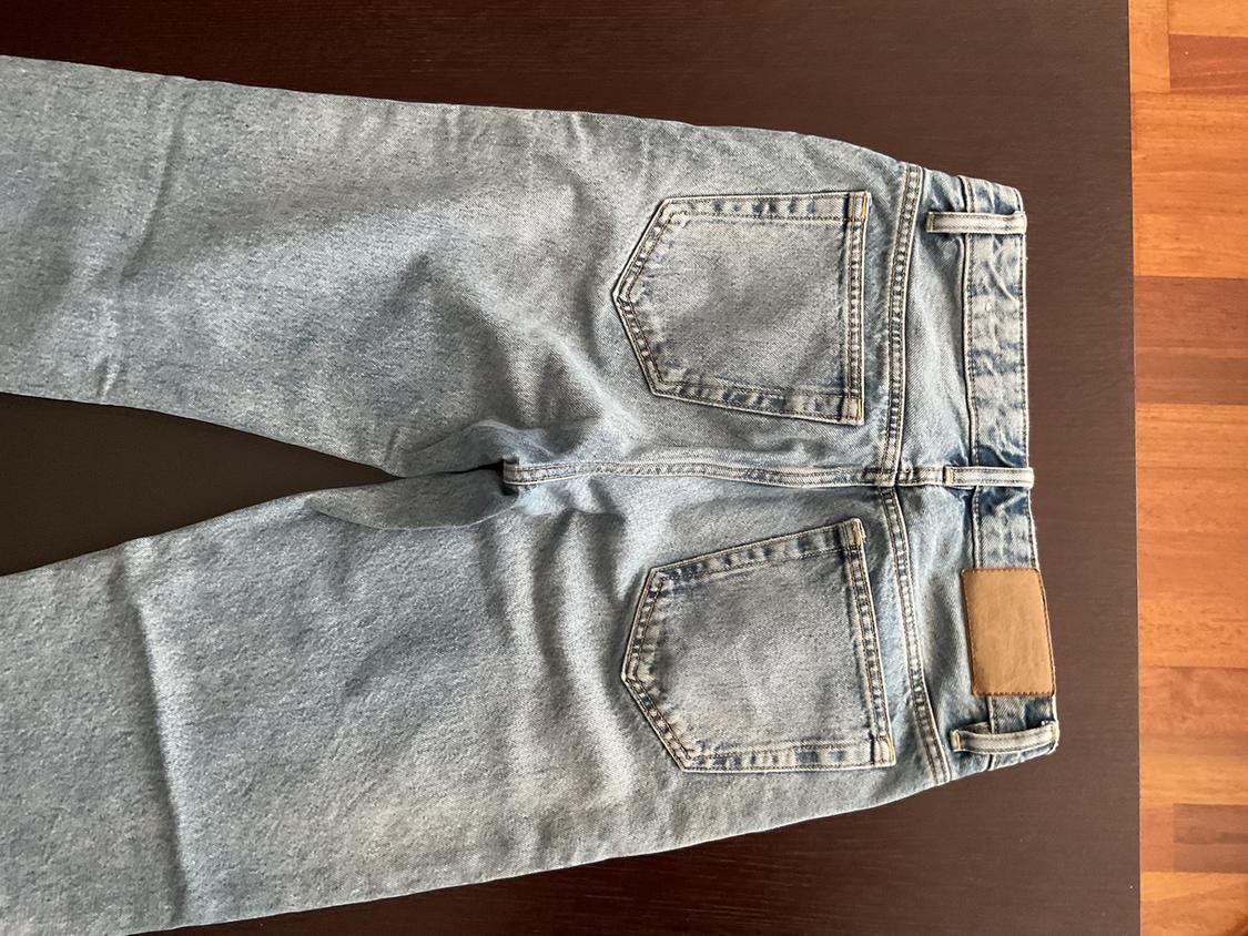 Light blue denim jeans with two back pockets and a brown label on the waistband, on a dark wooden surface.