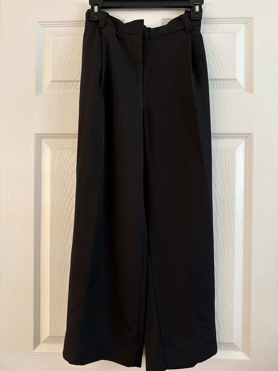 Black, wide-leg trousers hung on a white door, showcasing a classic and elegant design.
